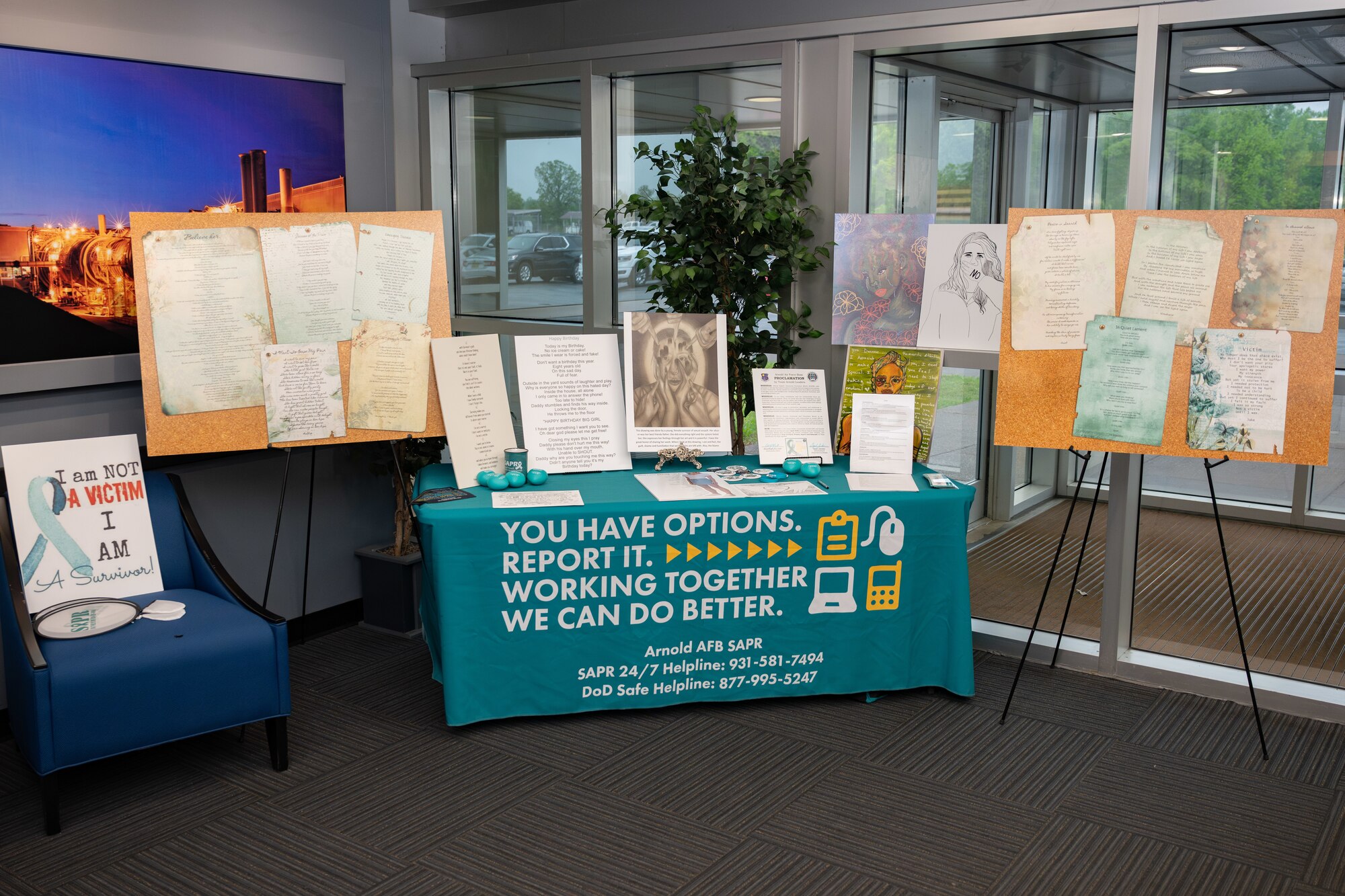 An art table showcasing numerous art pieces and poems written and drawn by sexual assault survivors along with a list of educational songs and movies surrounding sexual violence is displayed in the Test Operations Building at Arnold Air Force Base, Tenn., April 22, 2025. The display was set up by the Arnold AFB Sexual Assault Prevention and Response Office to coincide with Sexual Assault Awareness and Prevention Month, recognized each April, and was one of various events coordinated by the Arnold AFB SAPR team to coincide with SAAPM. (U.S. Air Force photo by Keith Thornburgh)