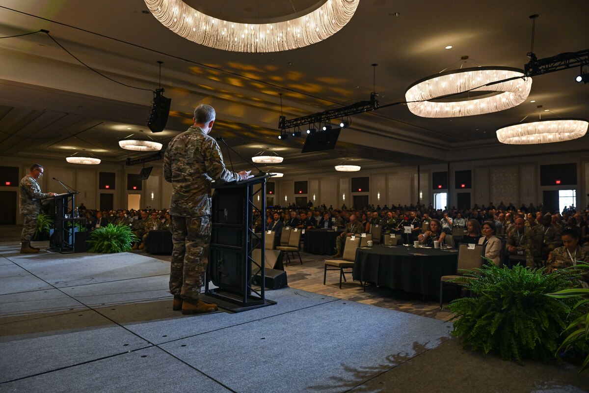 Two men speak on a stage as seen from the back.