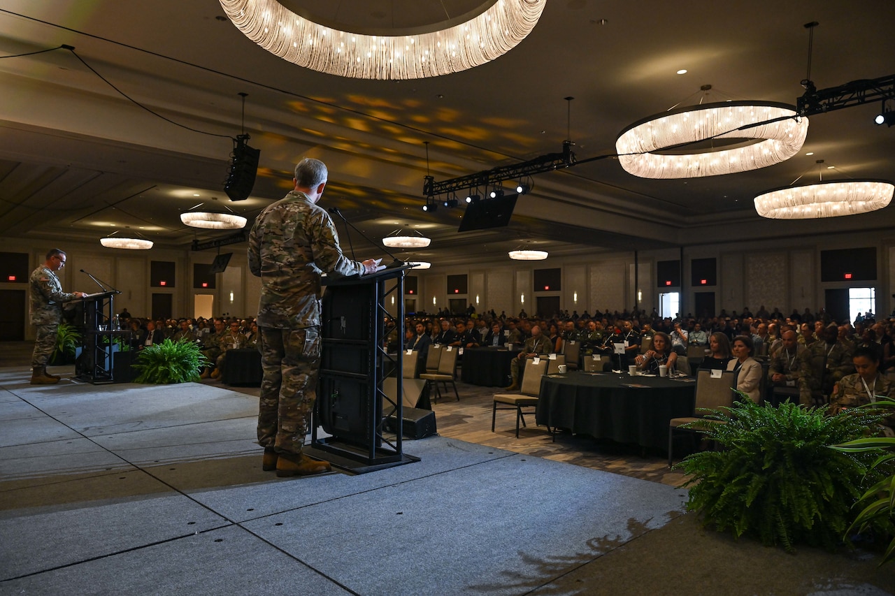 Two men speak on a stage as seen from the back.