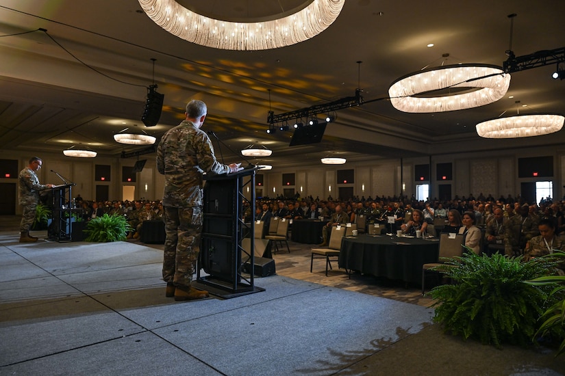 Two men speak on a stage as seen from the back.