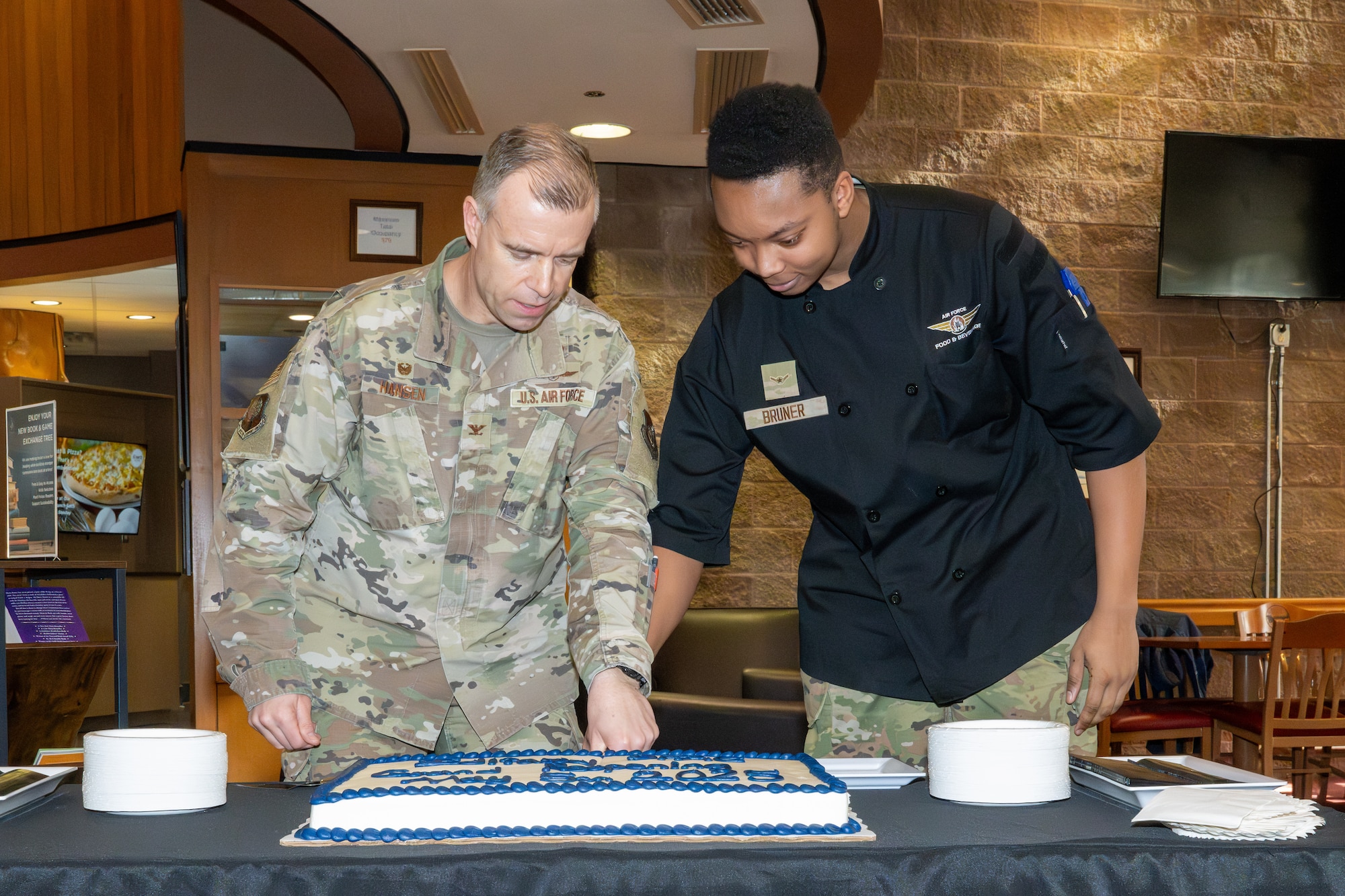 U.S. Air Force Col. Dustin Hansen, 673d Mission Support Group commander, and Airman Adrian Bruner, a food service apprentice assigned to the 673d Force Support Squadron, cut a cake celebrating an improved Iditarod Dining Facility at Joint Base Elmendorf-Richardson, Alaska, May 5.