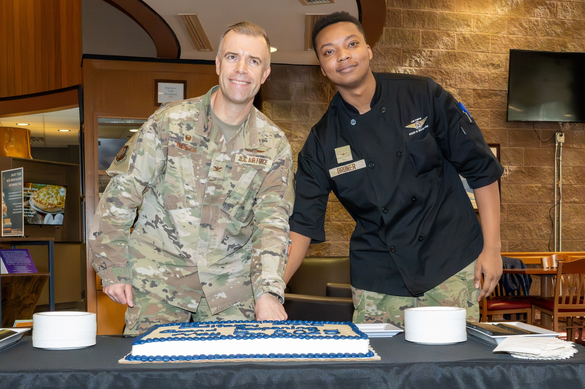 U.S. Air Force Col. Dustin Hansen, 673d Mission Support Group commander, and Airman Adrian Bruner, a food service apprentice assigned to the 673d Force Support Squadron, cut a cake celebrating an improved Iditarod Dining Facility at Joint Base Elmendorf-Richardson, Alaska, May 5.