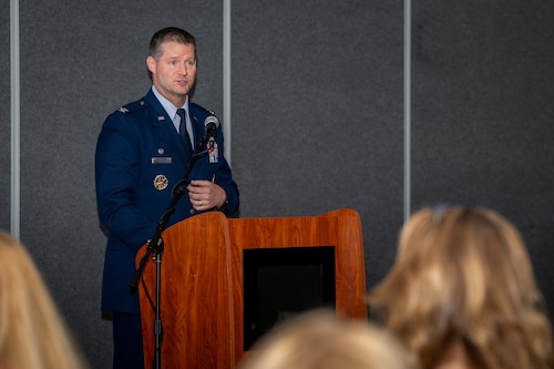 A man in a military service dress uniform stands behind a podium and microphone