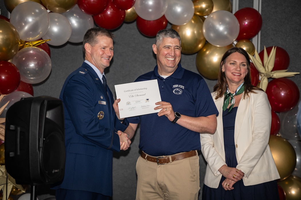 A man wearing a Penn State University polo and khakis, poses for a photo with a man in military service dress uniform, and brunette woman