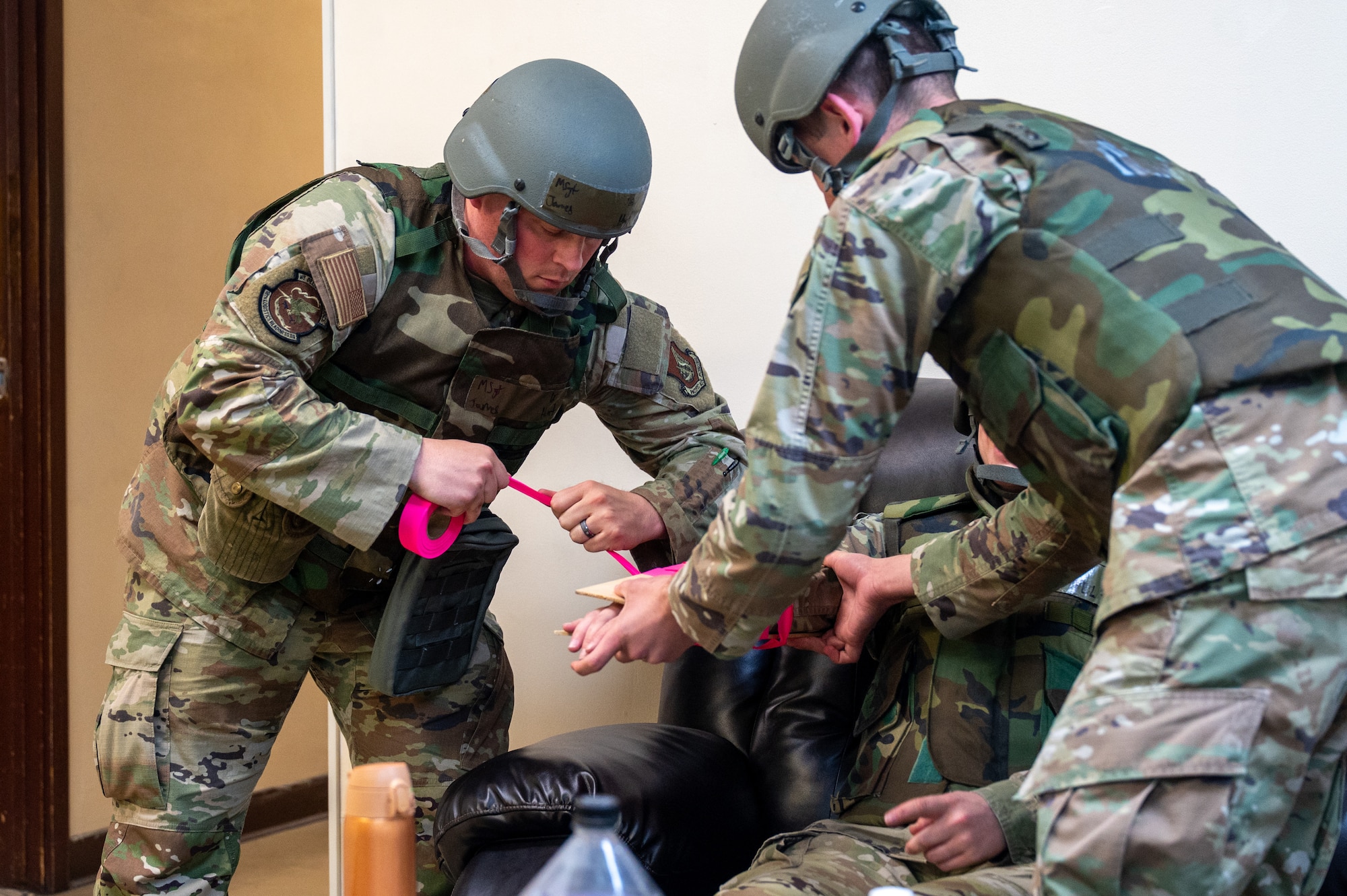 Air Force Airmen treat a simulated injury with creating a splint while wearing flack vest protective gear