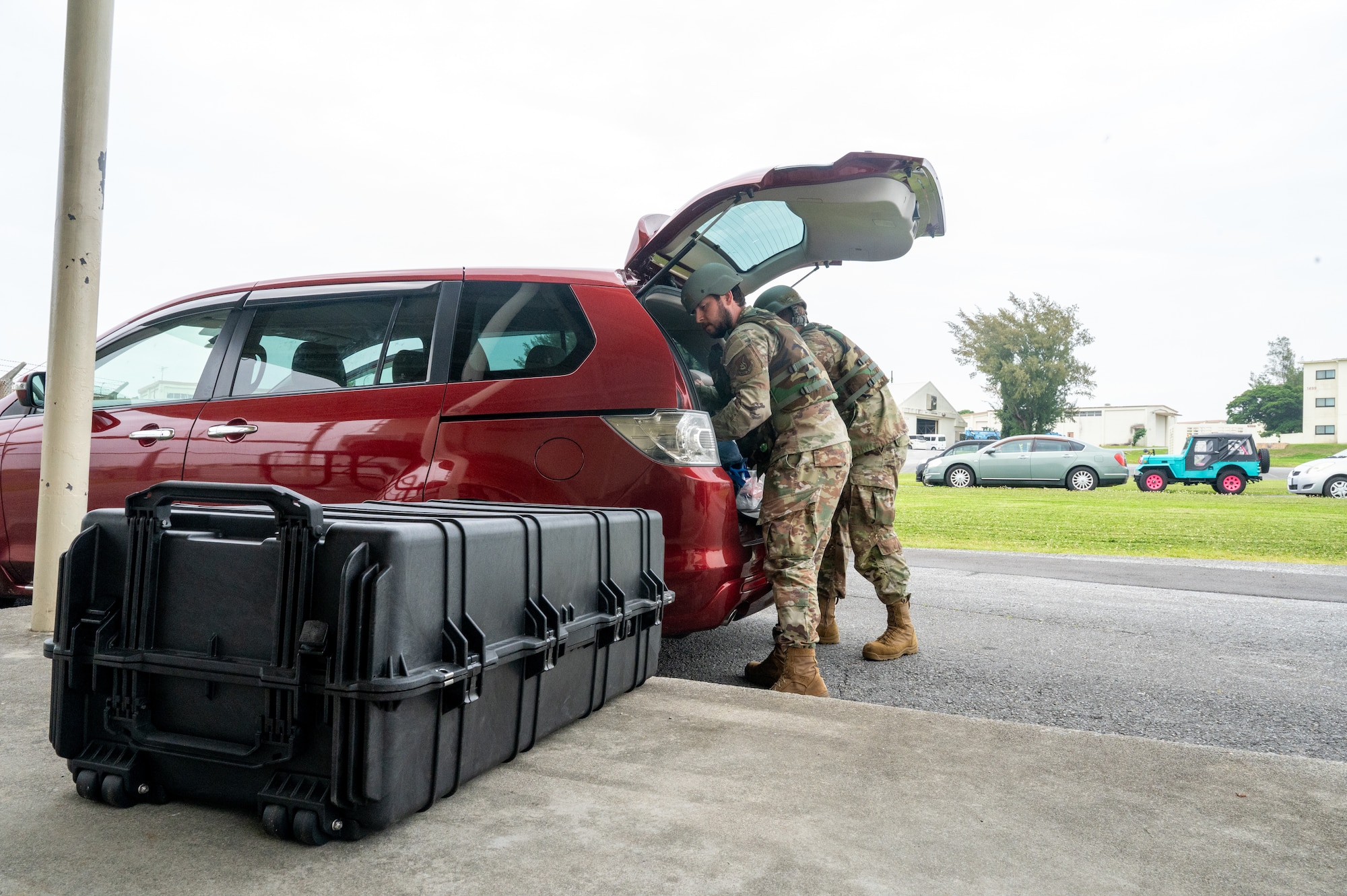 Air Force Airmen load up a red vehicles trunk with a black pelican case