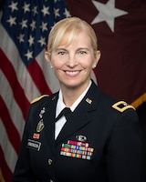 Female general officer posing for command photo in dress uniform with U.S. flag and her general officer flag in the background.