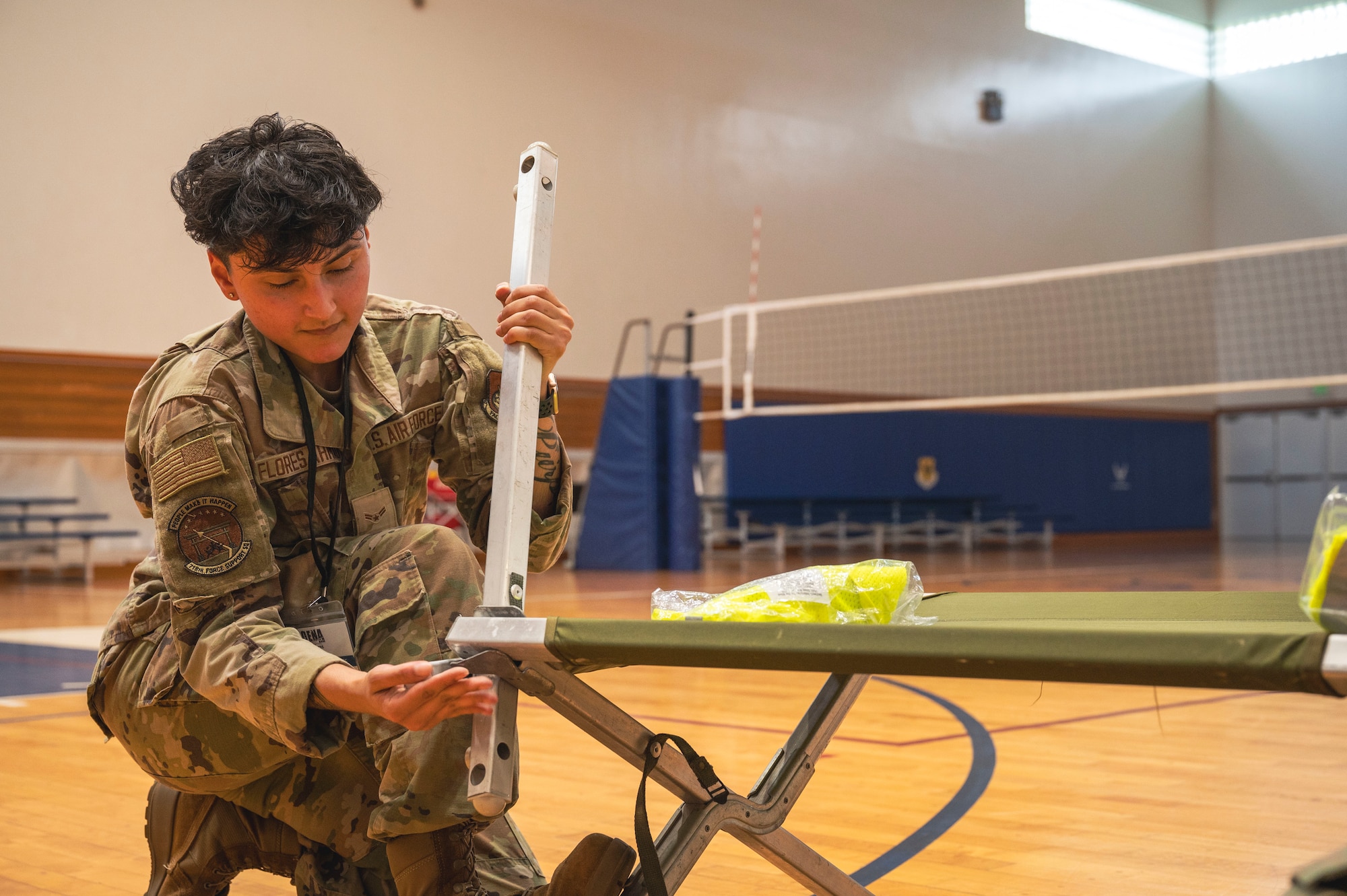 A Air Force Member assembles a cot for a medical exercise on a indoor basketball court