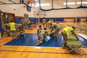 Air Force Members wearing reflective vests assemble cots for a medical exercise on a indoor basketball court