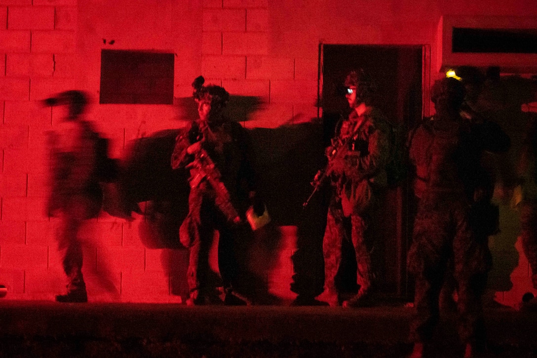 A group of Marines in tactical gear stand near a wall while surrounded by red lighting.