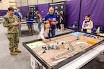 Capt. JD Crinklaw, commander, Puget Sound Naval Shipyard & Intermediate Maintenance Facility, and volunteer Tom Terry observe as two students from Cotton Wood Elementary School compete in the 3rd Annual Navy Peninsula Robotics Competition at North Kitsap High School in Poulsbo, Washington, April 29, 2025. (U.S. Navy photo by Jeb Fach)