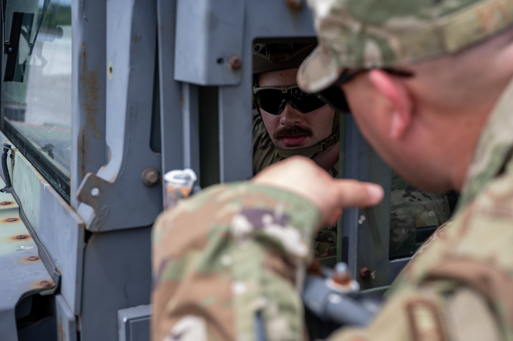 Military members talk to each other through the window of a front loader