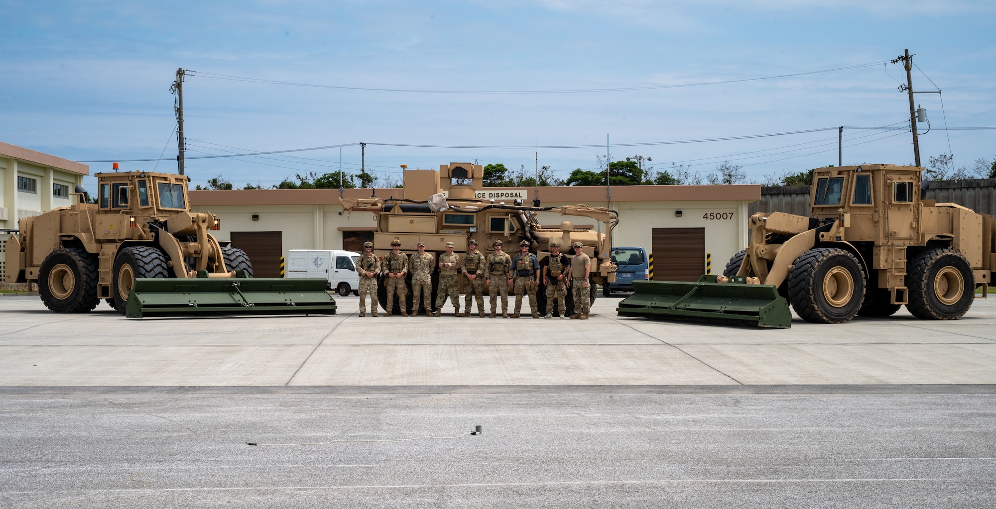 Military members pose for a photo on a flightline in front of three front loaders