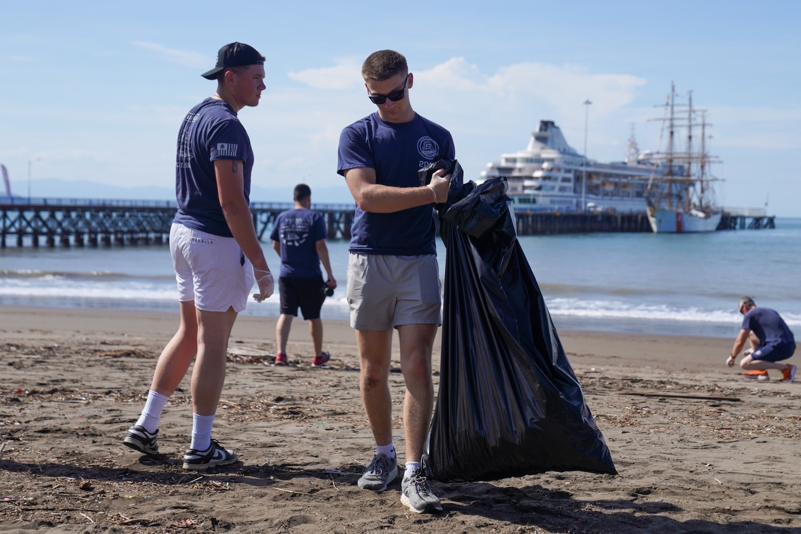 Two U.S. Coast Guard Barque Eagle (WIX 327) crew members collect trash on a local beach in Puntarenas, Costa Rica on April 27, 2025. For the first time since 2008, the Eagle sailed to the West Coast, making its first-ever port visit to Costa Rica, engaging with international partners and performing community service. (U.S. Coast Guard courtesy photo by U.S. Embassy Costa Rica.)