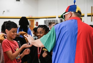 A magician hands a child a coin after performing a magic trick as another child watches.