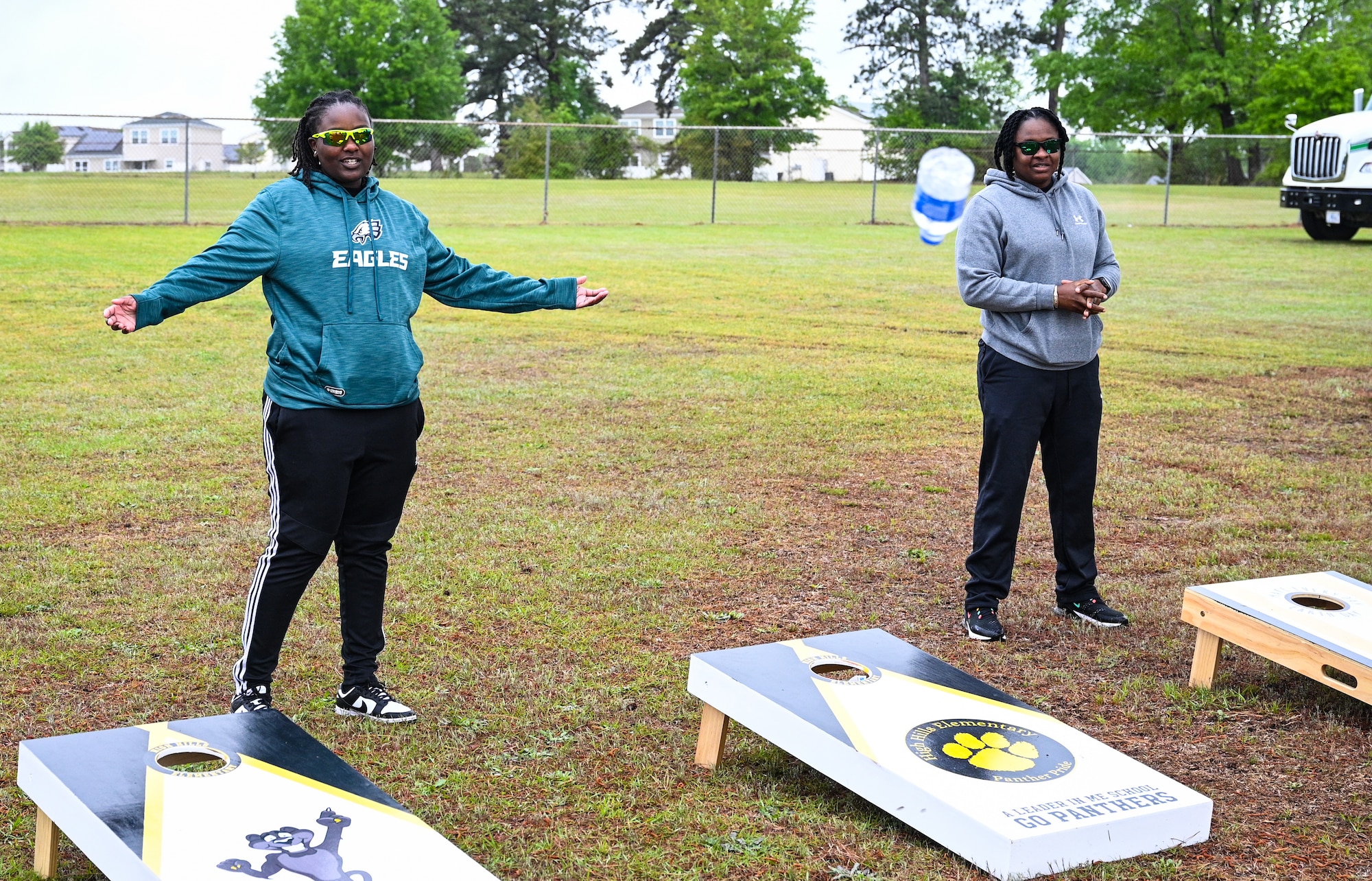 Two volunteers stand behind cornhole boards as students throw bottles in the holes to signify recycling.