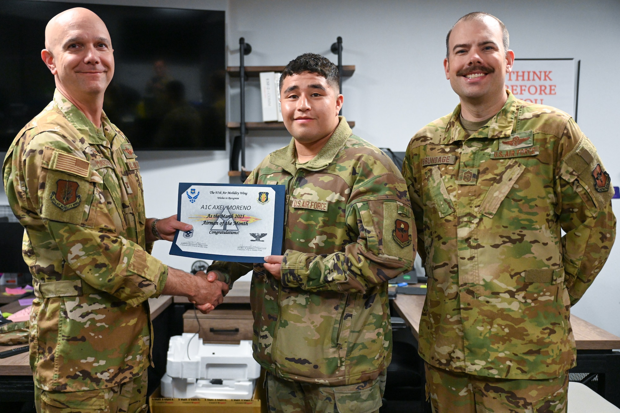 U.S. Air Force Col. Jeff Marshall, 97th Air Mobility Wing (AMW) commander, left, and Chief Master Sgt. Justin Brundage, 97th AMW command chief, right, awards Airman 1st Class Axel Moreno, 97th Communications Squadron (CS) client systems technician, at Altus Air Force Base, Oklahoma, April 24, 2025. The 97th CS develops and implements information technology solutions, provides knowledge management, information assurance, and communications security functions. (U.S. Air Force photo by Airman 1st Class Nathan Langston)