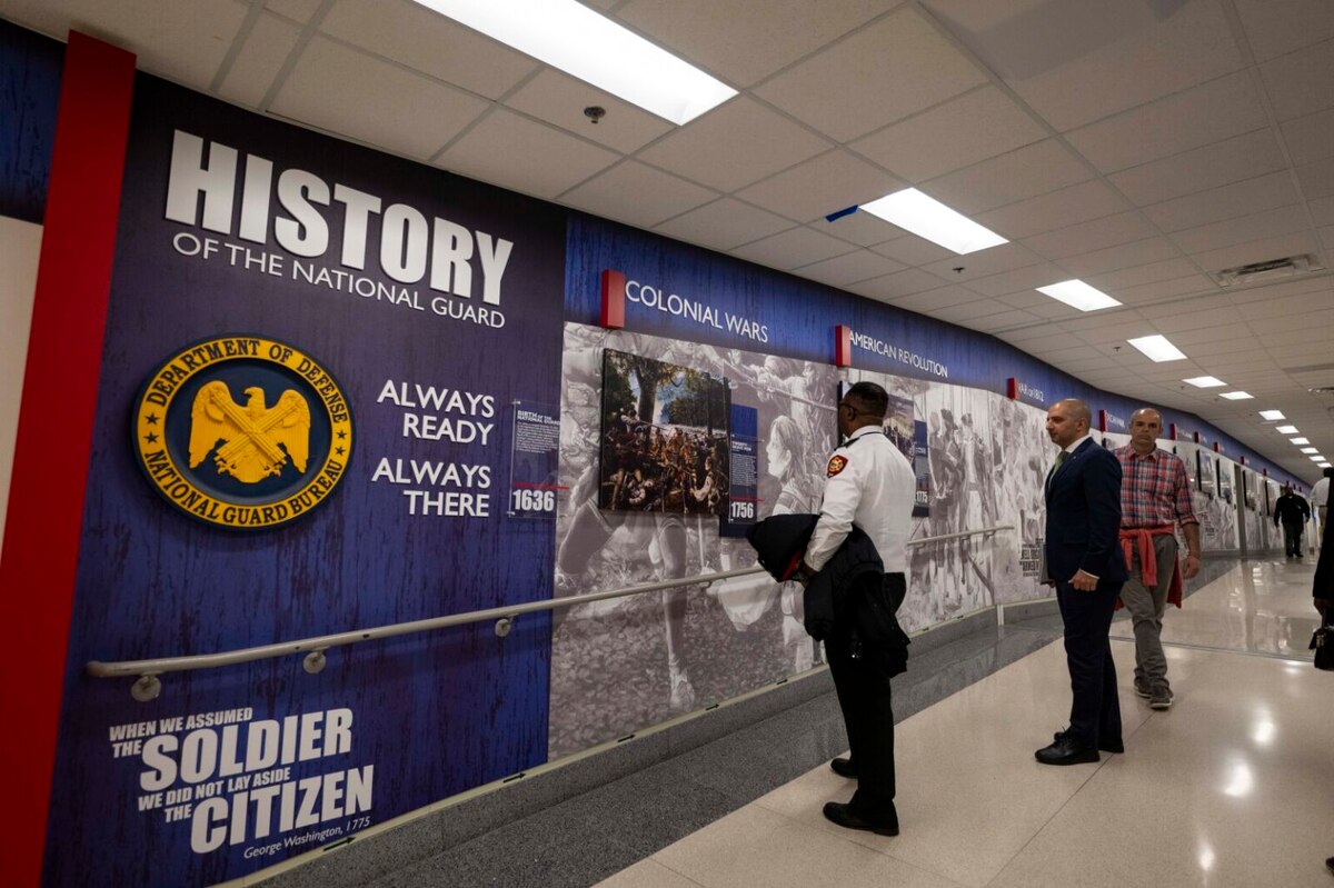 Individuals in business attire look at artwork on a wall with signs that read, "History of the National Guard."