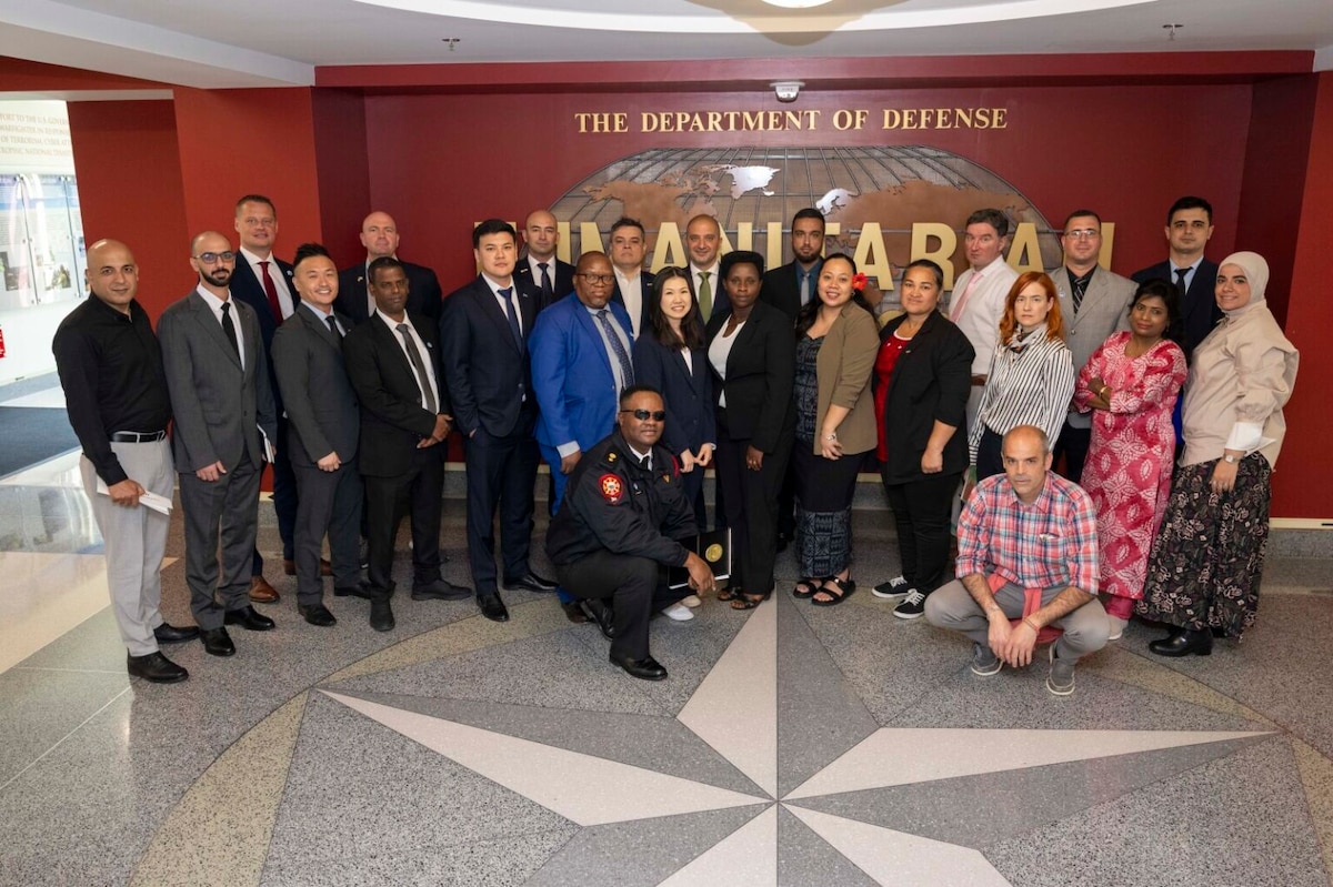 A large group of people in business attire stand in front of a wall that reads, "The Department of Defense."