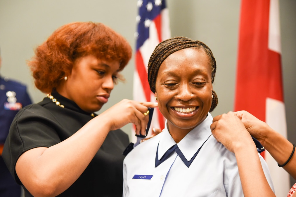 An airman has promotion insignia added to their uniform by two people as another person observes.