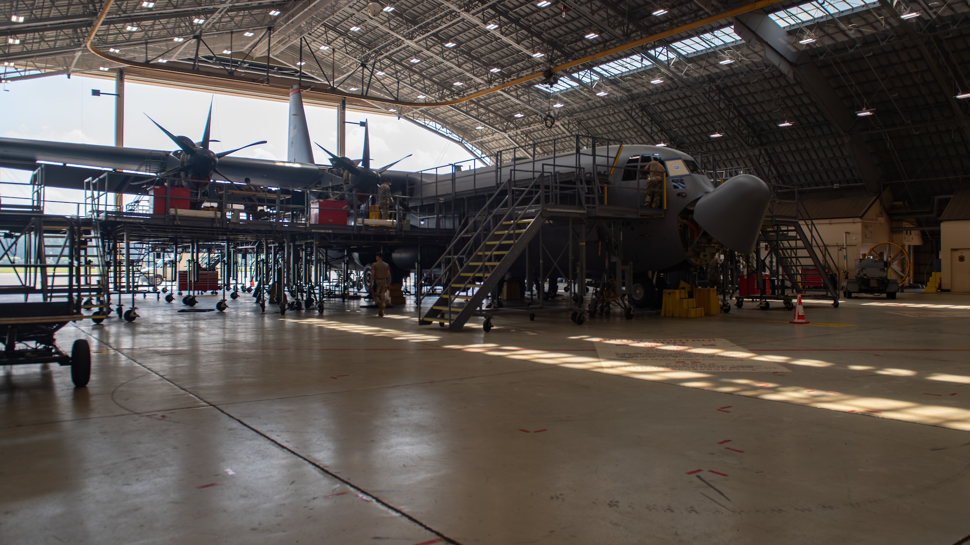 A gray C-130 J Super Hercules sits in a hanger with scaffolding and platforms used by maintenance surrounding it.