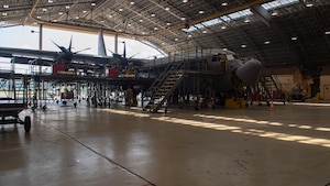 A gray C-130 J Super Hercules sits in a hanger with scaffolding and platforms used by maintenance surrounding it.