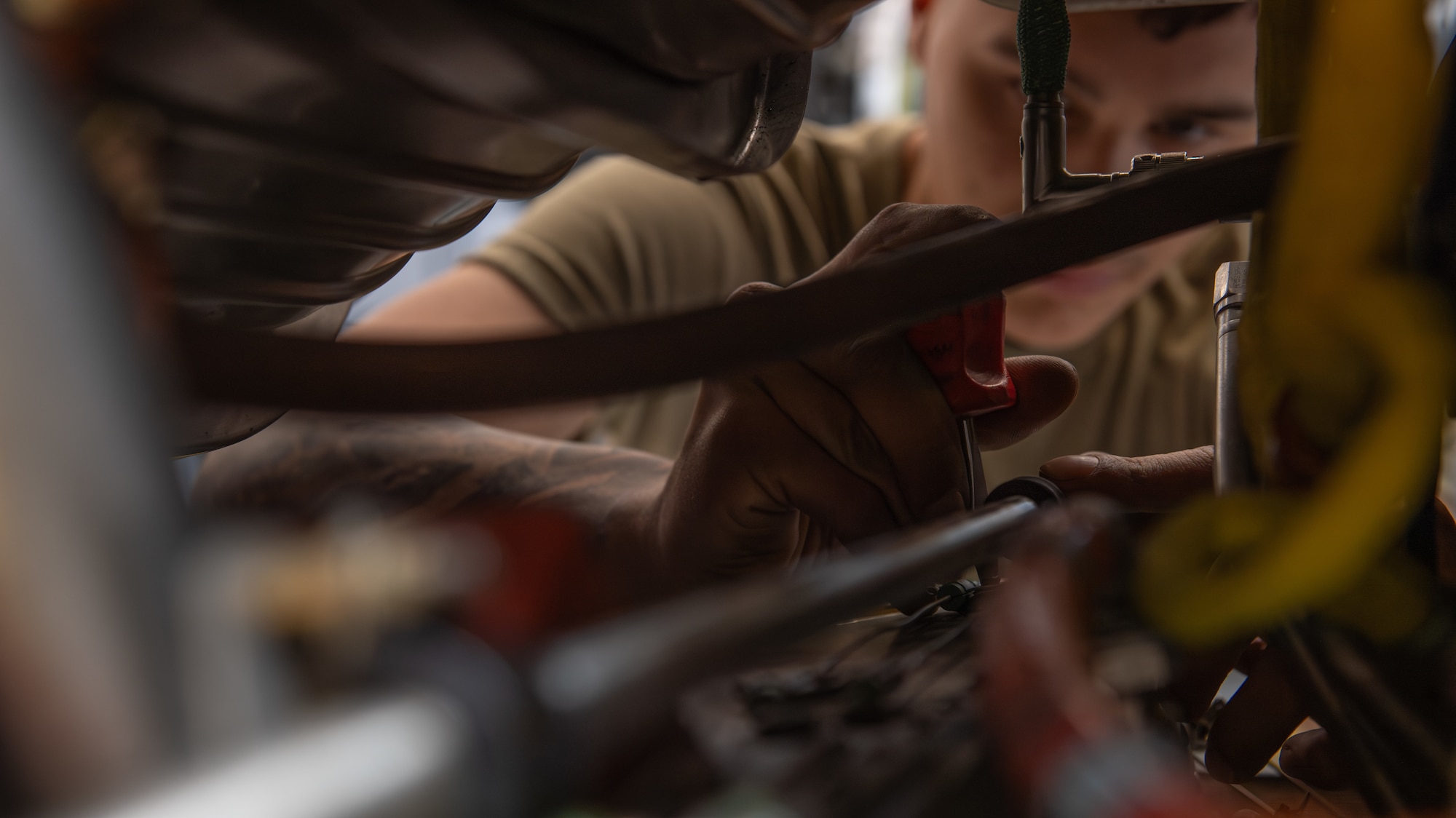 An Airman's hand and eyes are seen through an opening of C-130 J engine components, framing the subject.