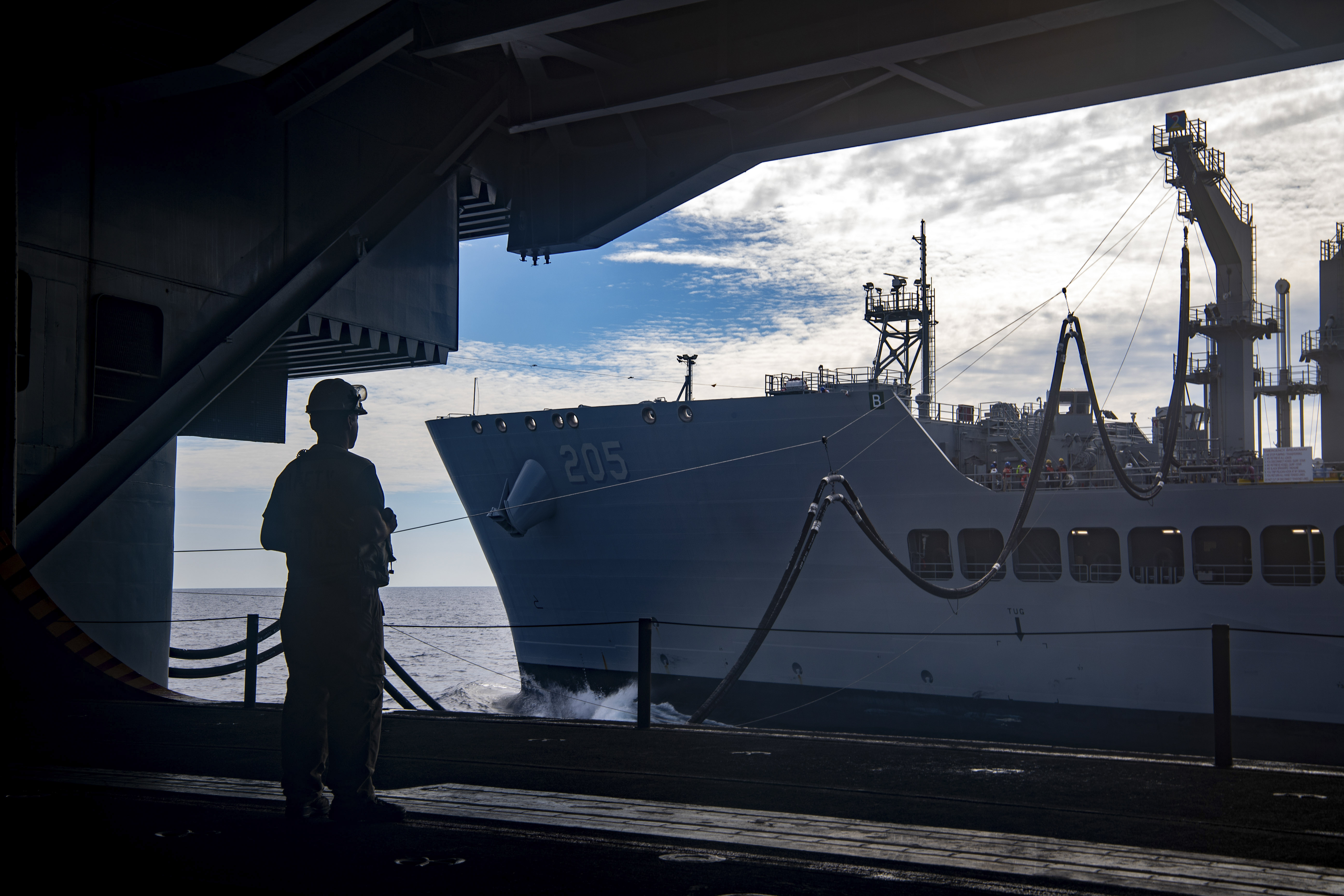 A Sailor observes a replenishment-at-sea with the fleet replenishment oiler USNS John Lewis (T-AO 205) in the hangar bay of the aircraft carrier USS Nimitz (CVN 68) in the South China Sea, May 5, 2025. The Nimitz is underway in the U.S. 7th Fleet area of operations on a scheduled deployment, demonstrating the U.S. Navy's unwavering commitment to a free and open Indo-Pacific. (U.S. Navy Photo by Mass Communication Specialist Seaman Apprentice Franklyn M. Guage)