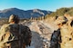 Soldiers conducting a patrol in Greece on a dirt road with a mountain range in front of them.