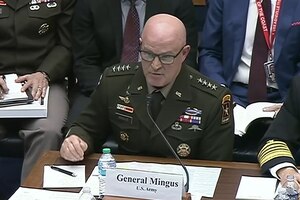 An Army general sits at a table and speaks into a microphone.