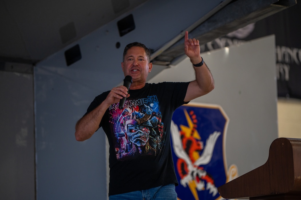 A man points his finger in the air while speaking on a microphone.