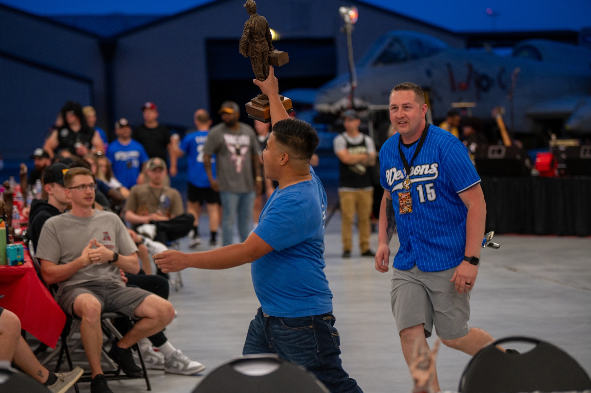 One man holds up his trophy after winning as another man runs up to congratulate the win.