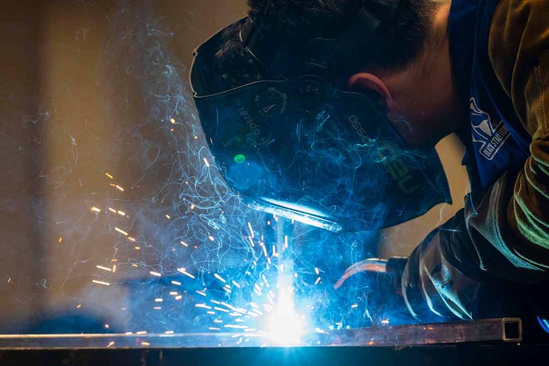 A close-up of sparks flying as an airman wearing protective gear welds metal.