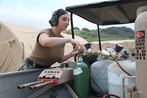 Interior Communications Electrician 1st Class Theodora Kales, battle effects technician with Naval Expeditionary Medicine Warfighter Development Center (NEMWDC), adjusts the oxygen pressure settings on a battle effects system used to simulate .50 caliber gunfire and explosions during an Expeditionary Resuscitative Surgical System course at NEMWDC, Apr. 14. The realistic soundscape enhances stress exposure and immersion for medical teams operating in combat-simulated environments. (U.S. Navy photo by Petty Officer 2nd Class Moira Francine Esquivel)