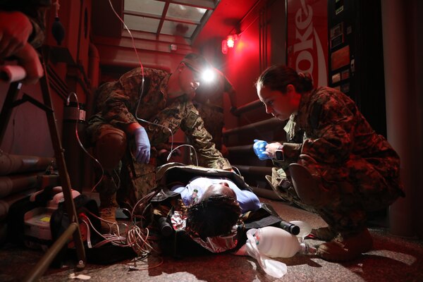 Lt. Joshua Grimes (left), physician assistant, and Lt. j.g. Ashton Hartwell (right), emergency room nurse, with Expeditionary Resuscitative Surgical System (ERSS) 7 assess a simulated drowning patient played by Logistic Specialist Seaman Audrey Bangura with Naval Expeditionary Medicine Warfighter Development Center (NEMWDC) during an ERSS course at NEMWDC, Apr. 14. The scenario incorporates realistic moulage, role players, and battlefield effects to enhance trauma response and prepare EXMED teams for operational deployment in austere environments. (U.S. Navy photo by Petty Officer 2nd Class Moira Francine Esquivel)