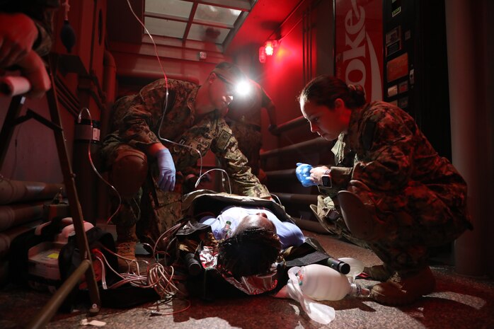 Lt. Joshua Grimes (left), physician assistant, and Lt. j.g. Ashton Hartwell (right), emergency room nurse, with Expeditionary Resuscitative Surgical System (ERSS) 7 assess a simulated drowning patient played by Logistic Specialist Seaman Audrey Bangura with Naval Expeditionary Medicine Warfighter Development Center (NEMWDC) during an ERSS course at NEMWDC, Apr. 14. The scenario incorporates realistic moulage, role players, and battlefield effects to enhance trauma response and prepare EXMED teams for operational deployment in austere environments. (U.S. Navy photo by Petty Officer 2nd Class Moira Francine Esquivel)