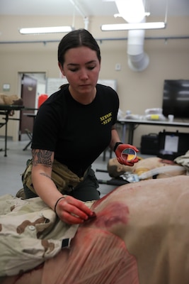 Hospital Corpsman 3rd Class Abbigail Dunlap, moulage technician with Naval Expeditionary Medicine Warfighter Development Center (NEMWDC), applies bruise makeup on a high-fidelity manikin during an Expeditionary Resuscitative Surgical System course at NEMWDC, Apr. 14. The realistic wounds help immerse students in combat medical simulations and reinforce rapid trauma assessment skills. (U.S. Navy photo by Petty Officer 2nd Class Moira Francine Esquivel)
