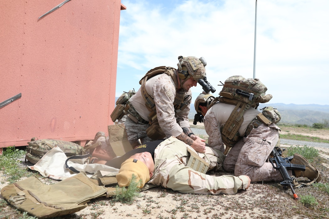 Special Operations Independent Duty Corpsman (SOIDC) Chief Hospital Corpsman Simon Trujillo and Hospital Corpsman 1st Class Nicholas Farris with 1st Reconnaissance Battalion, assess Culinary Specialist 2nd Class Raymond Santiago, a role player with Naval Expeditionary Medicine Warfighter Development Center (NEMWDC), after a simulated motor vehicle accident during an Expeditionary Resuscitative Surgical System (ERSS) course at NEMWDC, Apr. 14. The scenario incorporates realistic moulage, role players, and battlefield effects to enhance trauma response and prepare EXMED teams for operational deployment in austere environments. (U.S. Navy photo by Petty Officer 2nd Class Moira Francine Esquivel)