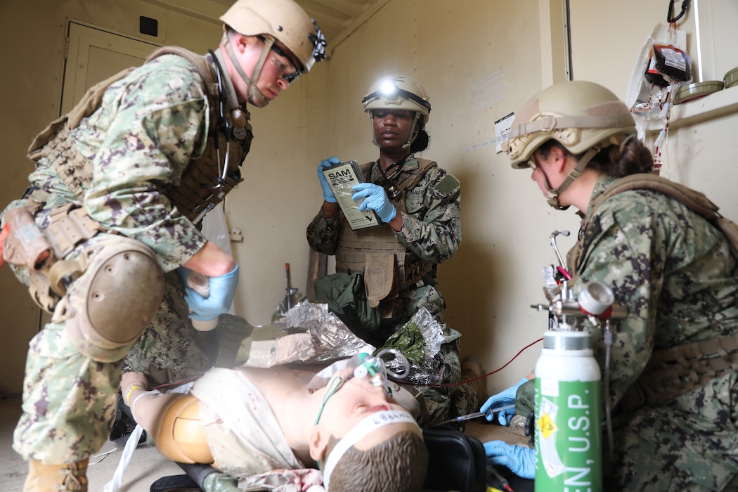 Lt. Joshua Grimes (left), physician assistant, Lt. j.g. Ashton Hartwell (right), emergency room nurse, and respiratory technician Hospital Corpsman 2nd Class Nya Jobs (center) with Expeditionary Resuscitative Surgical System (ERSS) 7prepare to put a splint on a simulated high-fidelity manikin during an ERSS course at Naval Expeditionary Medicine Warfighter Development Center, Apr. 14. The scenario incorporates realistic moulage, role players, and battlefield effects to enhance trauma response and prepare medical personnel for operational deployment in austere environments. Hospital corpsman 2nd Class Jobs says, “The sounds and gunshots definitely make it more realistic. I think the transport also made it realistic being in the back of a truck and in how much time it would take to get from one place to another instead of just running up and down the street, you guys really had us in the mountain and in the town.” (U.S. Navy photo by Petty Officer 2nd Class Moira Francine Esquivel)