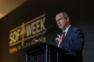 A man in a business suit is standing at a podium, gesturing with his hands.