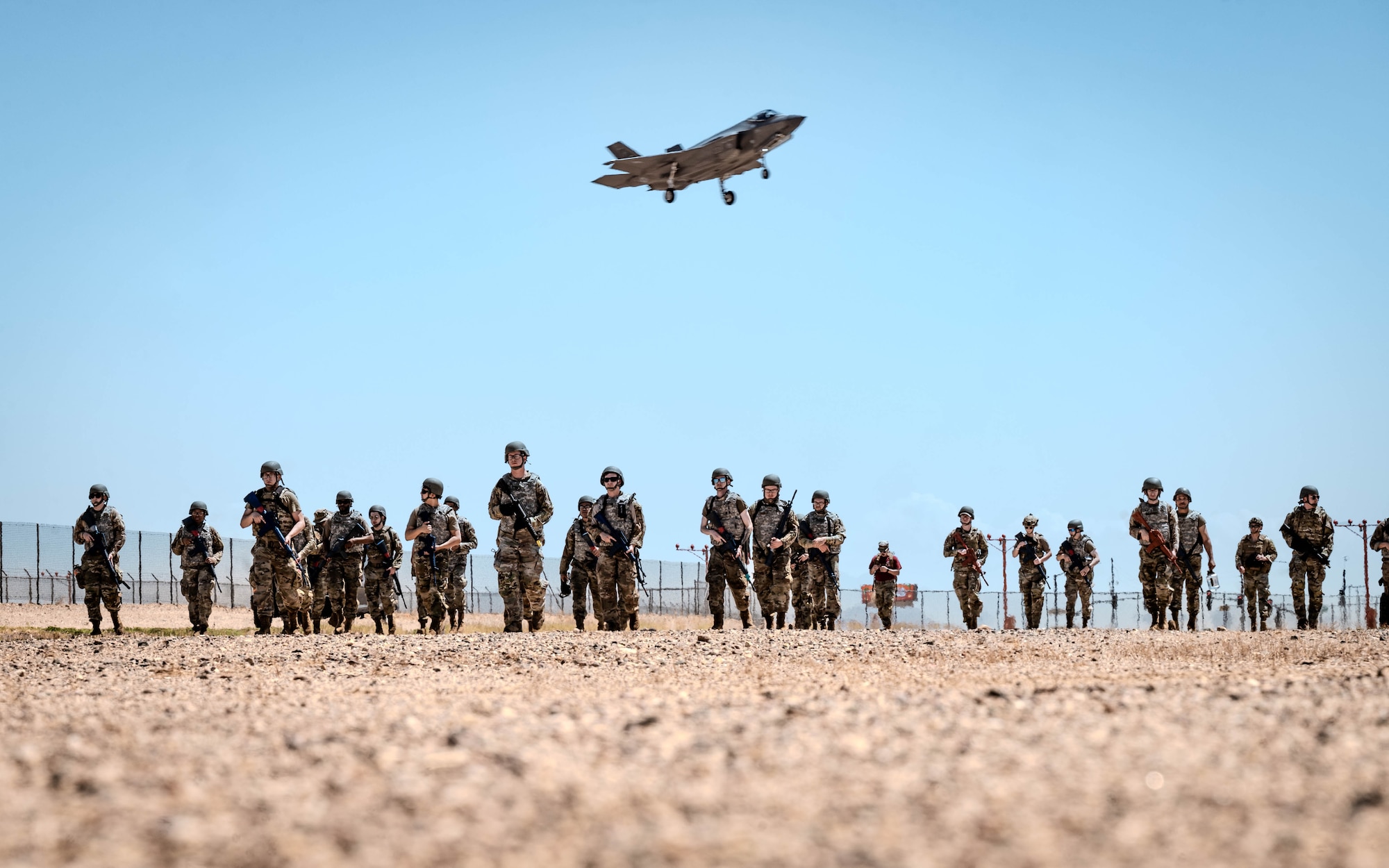U.S. Air Force Airmen attending the John. J Rhoades Airman Leadership School march to a forward operating point near the flightline as an F-35A Lightning II prepares to land.