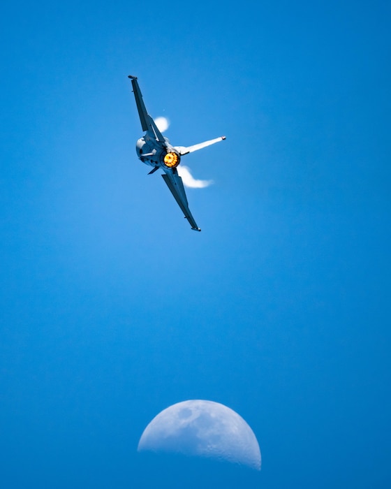 fighter jet flies in front of the moon in the background