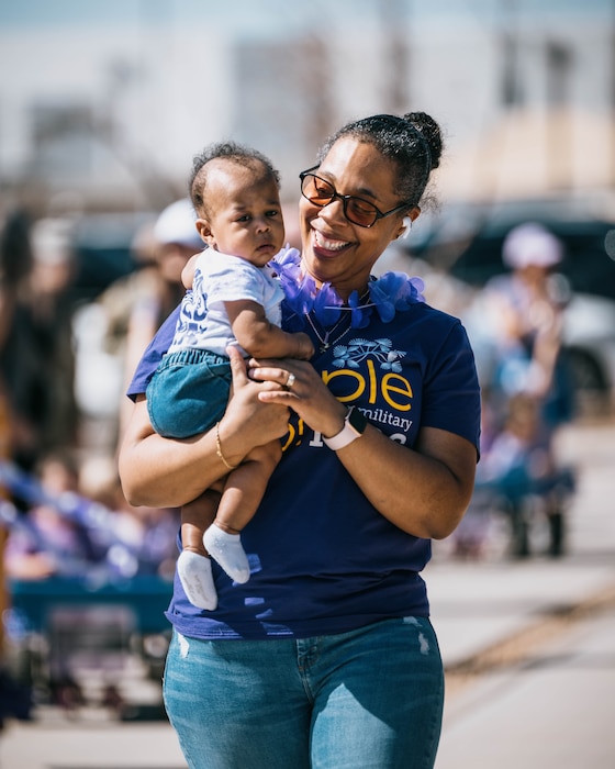 U.S. Air Force Master Sgt. April Ferrar, 56th Force Support Squadron military personnel flight chief, smiles while holding her baby during the Purple Up parade, April 25, 2025, at Luke Air Force Base, Arizona.