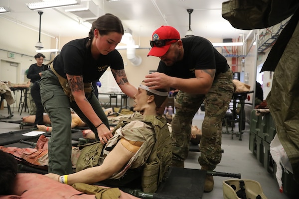Construction Electrician 1st Class Jason Gomes (right) and Hospital Corpsman 3rd Class Abbigail Dunlap (left) moulage technician and lead construction electrician instructor at Naval Expeditionary Medicine Warfighter Development Center (NEMWDC), put a flak vest onto a high-fidelity manikin during an Expeditionary Resuscitative Surgical System course at NEMWDC, Apr. 14. The realistic wounds and outfits help immerse students in combat medical simulations and reinforce rapid trauma assessment skills. (U.S. Navy photo by Petty Officer 2nd Class Moira Francine Esquivel)