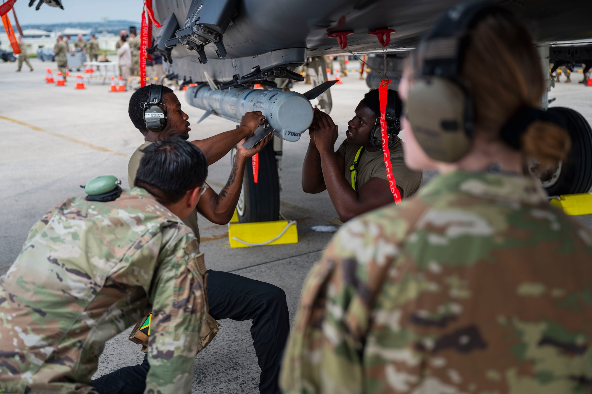 U.S. Air Force Senior Airman Semar Edwards, back left, 336th Fighter Generation Squadron load crew member,  and Senior Airman Fredarious Martin, back right, 336th FGS load crew member, affix tail fins to a munition on an F-15E Eagle