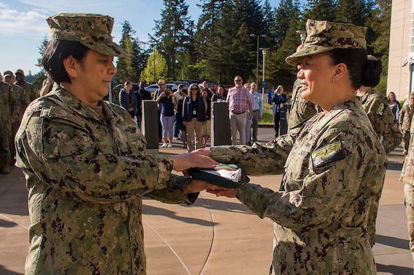 Capt. Maria Edusada, outgoing director of Navy Medicine Readiness Training Command Bremerton’s Directorate of Administration, is presented a ceremonial folded directorate for administration flag from recently retired Senior Chief Hospital Corpsman Arlene Alonzo, as a favor returned after having Edusada as the presiding officer at her retirement ceremony. (Official Navy photo by Mass Communication Specialist 2nd Class Jennifer Benedict, NHB/NMRTC Bremerton public affairs).