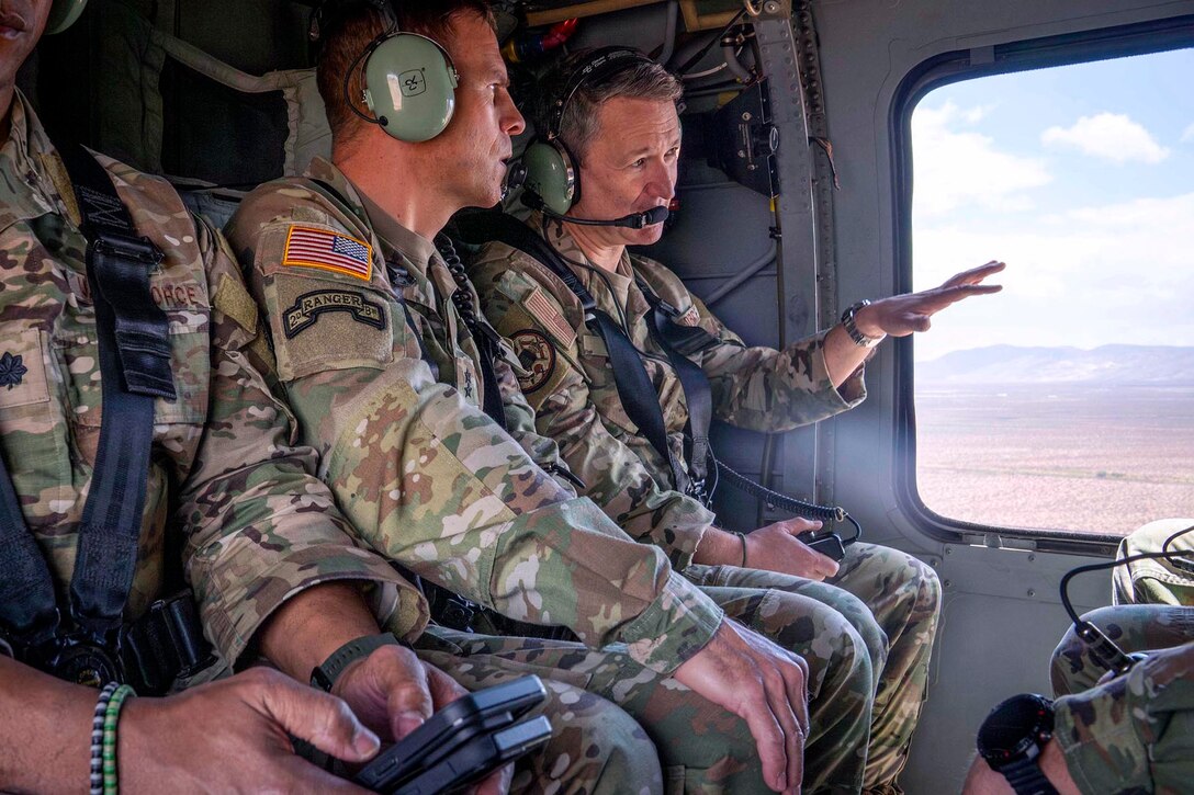 A military leader speaks to a soldier aboard the cabin of a helicopter wearing a headset.