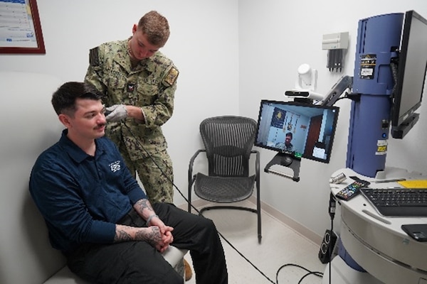 250401-N-FT324-4925. ROTA, Spain. HM3 Callum Wilkerson and HM3 Sean File, corpsmen at the Telehealth and Medical Home Port Clinic, demonstrate a physical assessment using the Telehealth Medical Cart, which enables real-time image sharing for remote provider evaluations. (U.S. Navy Photo by Lt. Cmdr. Alicia Sacks)