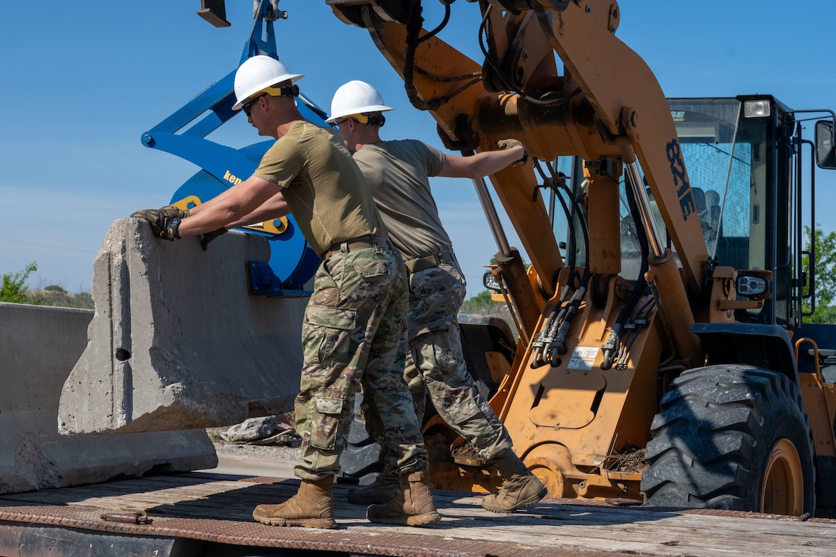 From left, Staff Sgt. Austen Windle and Airman 1st Class Hesston Garver, 22nd Civil Engineer Squadron pavements and construction equipment technicians, guide concrete barrier on the back of a truck in coordination with Lethal Stack at McConnell Air Force Base, Kansas, May 5, 2025. These Airmen are responsible for maintaining and constructing airfields, roads, and other infrastructure on bases and in deployed locations. (U.S. Air Force photo by Senior Airman Felicia Przydzial)