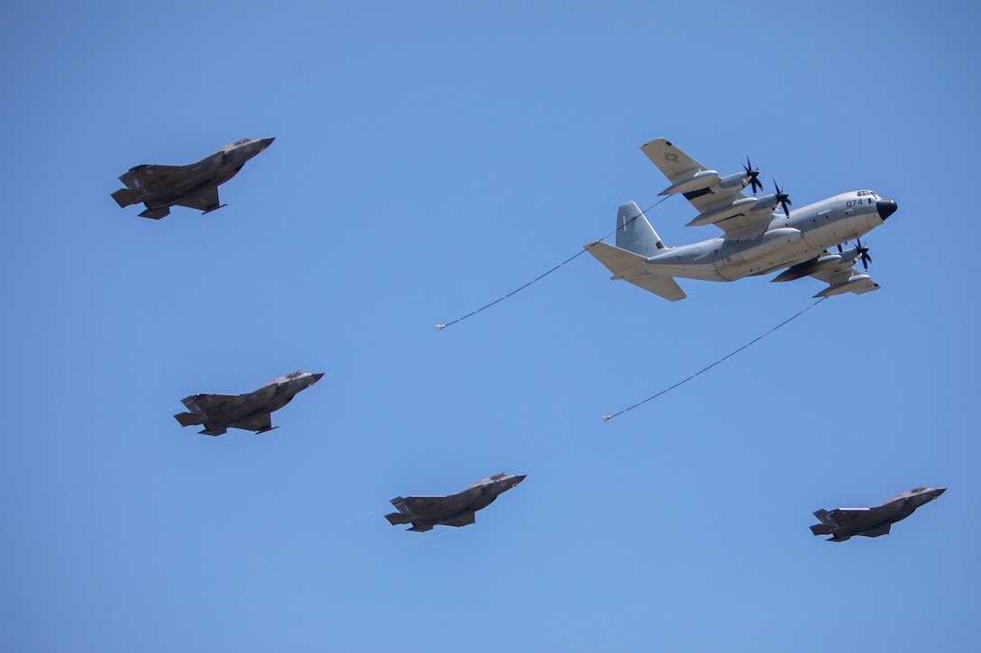 An aircraft extends two lines as four other aircraft fly behind it against a blue sky.